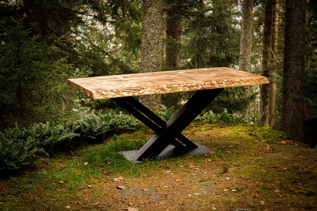 Ein angeflammter Massivholz-Tisch mit schwarzem Metallgestell steht mitten im Wald